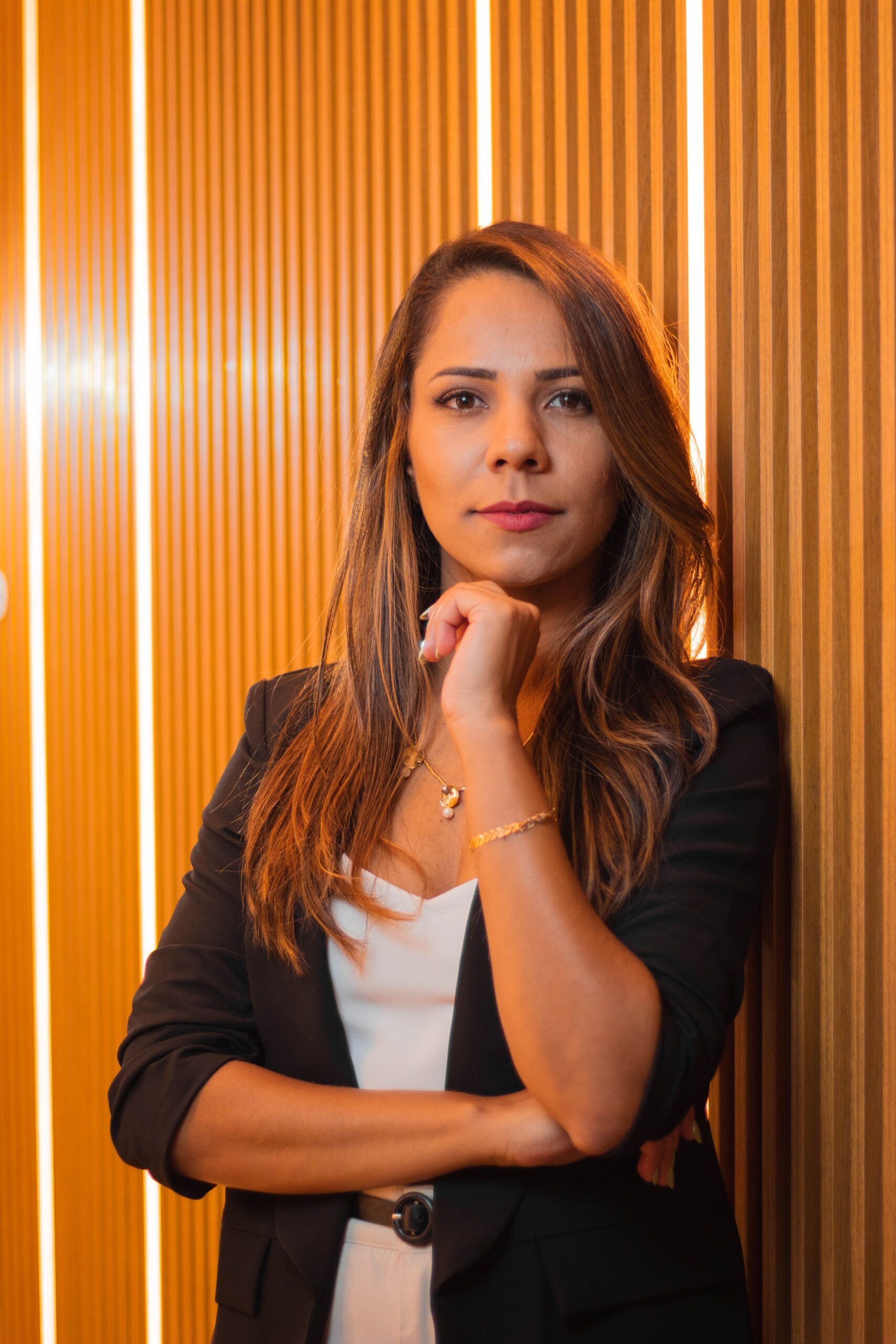 A confident businesswoman posing elegantly against a modern wooden wall indoors.